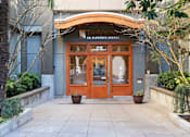 Thumbnail 19 of 22 - A building with a brown door and windows surrounded by green plants.