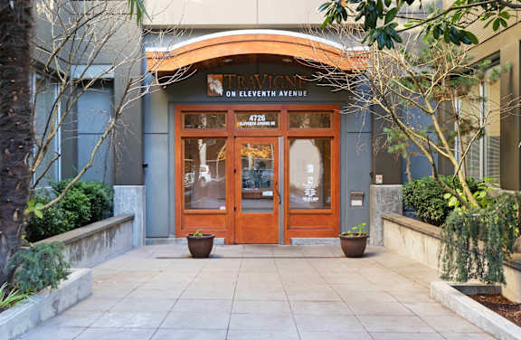 A building with a brown door and windows surrounded by green plants.
