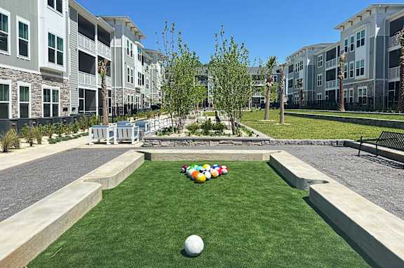 A grassy area with a ball and a row of multicolored balls in front of apartment buildings.