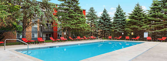 A swimming pool surrounded by trees and chairs.