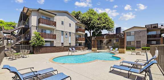 A swimming pool surrounded by trees and chairs in a residential area.