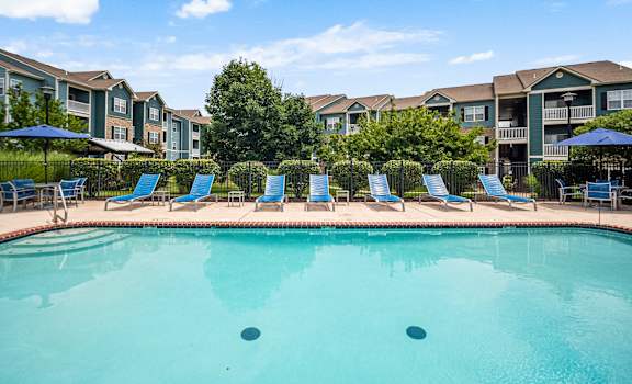 A swimming pool surrounded by lounge chairs and umbrellas in front of apartment buildings. at Aventura at Richmond, St. Peters