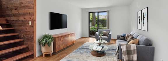 A living room with a grey couch, a coffee table, and a flat screen TV mounted on the wall.