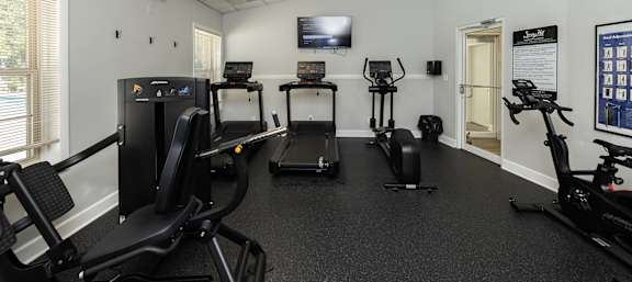 A gym room with exercise equipment and a television.