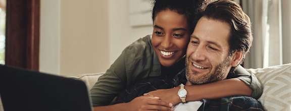 A man and woman are sitting on a couch with a laptop.