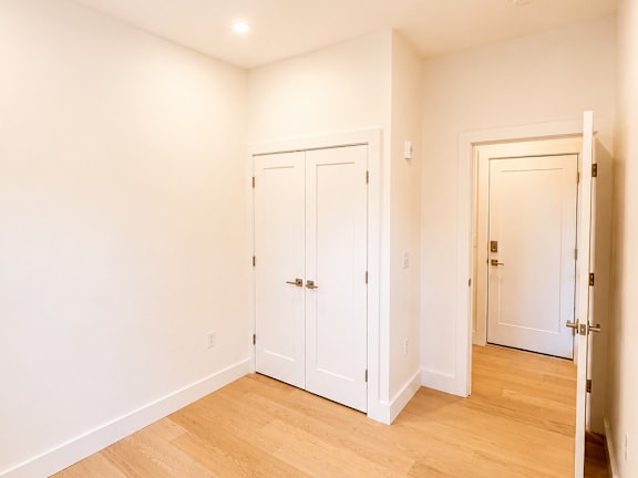 A room with white walls and wooden flooring with three doors.