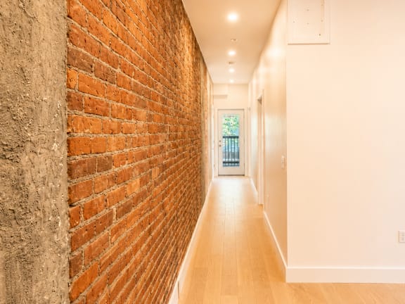A long hallway with a brick wall on the left and wooden floors.