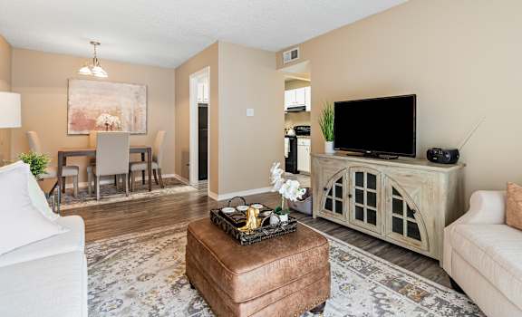 A living room with a white couch, a brown ottoman, and a television on a cabinet.