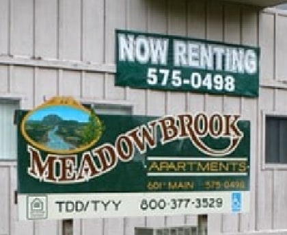 A sign for Meadowbrook Apartments is displayed in front of a building.
