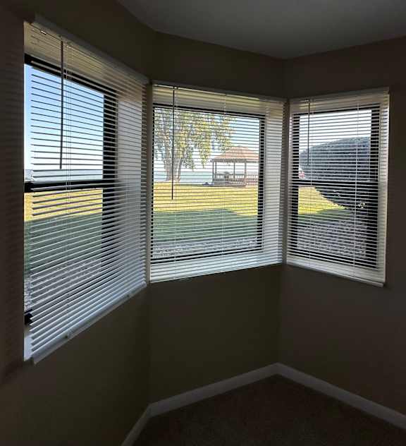 A room with three windows covered in white blinds.