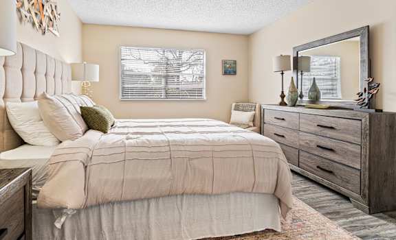 A bedroom with a large bed, a mirror, and a wooden dresser.