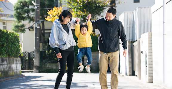 A man and woman are walking with a child who is jumping in the air.