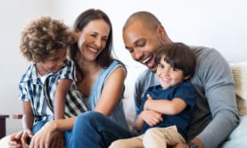A family of four is sitting together on a couch.