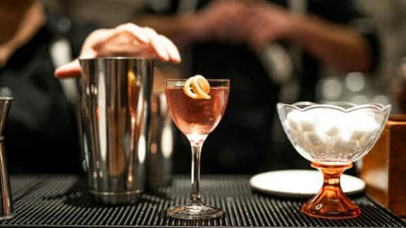 a cocktail glass with a orange garnish on a bar