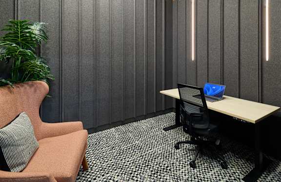 A modern office with a wooden desk, a black chair, and a pink armchair.