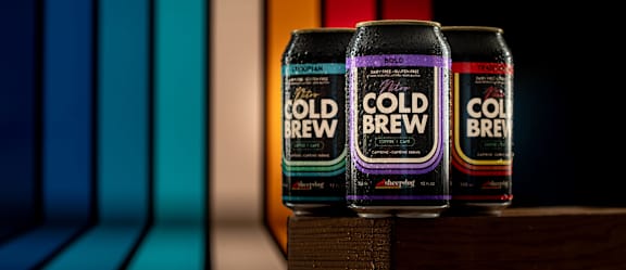 Three cans of Cold Brew are displayed on a wooden surface.