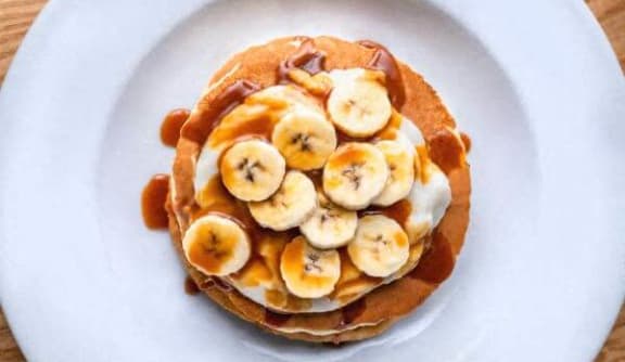 a stack of pancakes with bananas and syrup on a white plate