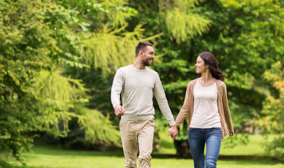 A man and a woman are walking hand in hand in a park.