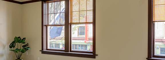 A room with a carpeted floor, a ceiling fan, and two windows.
