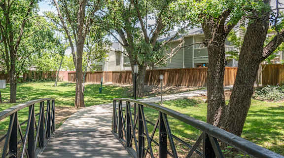 a wooden bridge in a park with trees and a building in the background