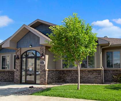 The beautiful exterior of the front office building and the green space with grass, trees, and shrubs at Willison Garden Apartment Homes. 