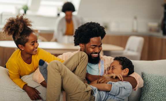 A family of three is sitting on a couch in a living room.