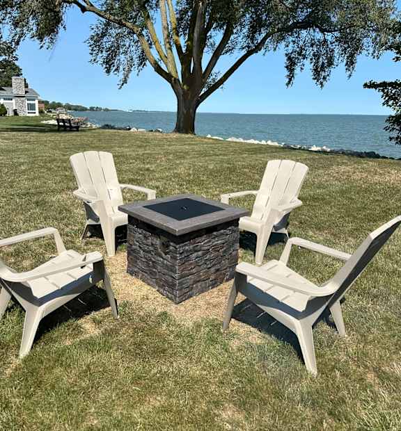 A fire pit surrounded by three chairs on a lawn.