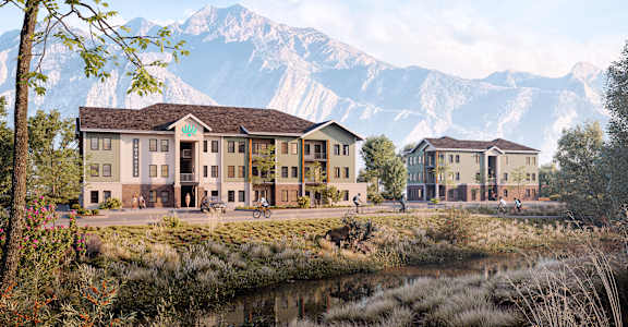 A modern building with a brown roof is situated by a body of water with mountains in the background.