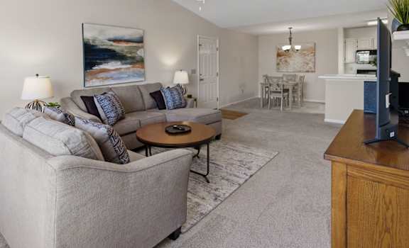 A living room with a grey couch and a painting on the wall.