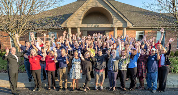 A group of people are standing in front of a building with their hands raised.