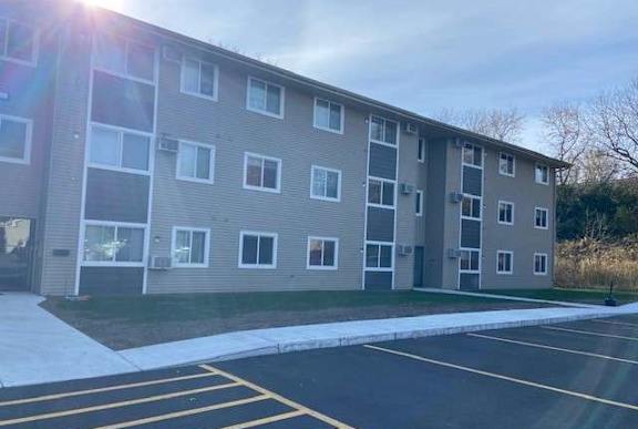 A sunny day at the apartment complex with a parking lot in front.