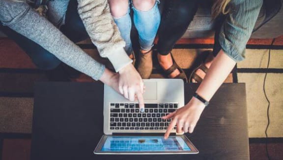 a group of people sitting around a laptop computer