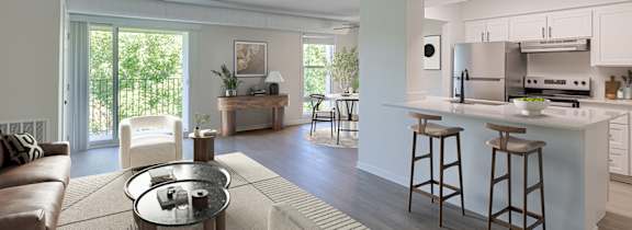 A living room with large windows and a view into the kitchen