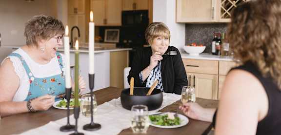 Three women are sitting at a table with plates of food and glasses of wine.