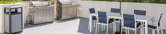a patio with a table and chairs and two bbq grills