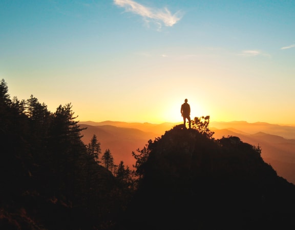 Man in Silhouette Standing In Front of the Sun on Mountain