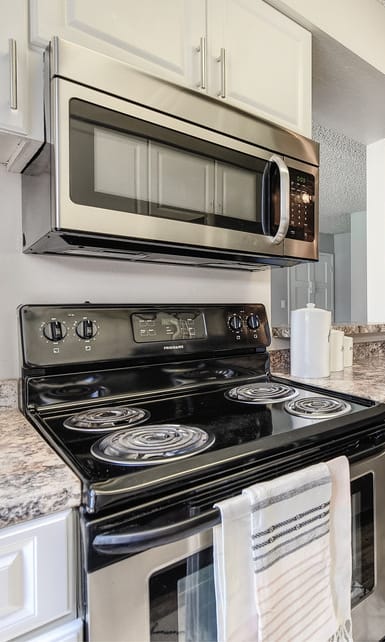 Galley style kitchen with white upper and lower cabinets. Stainless steel electric appliances. Over stove built in microwave.