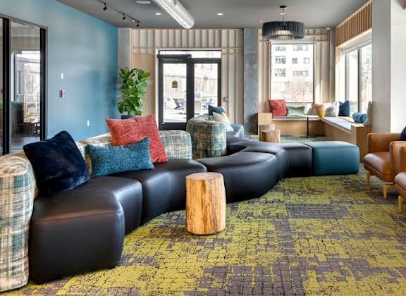 A large room with a long black couch and a green rug.