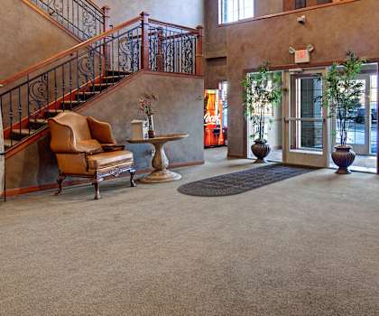 The front lobby with a grand entrance featuring a staircase, comfortable leather chairs, plants, coffee tables, and a vending machine at Grand River Estates. 