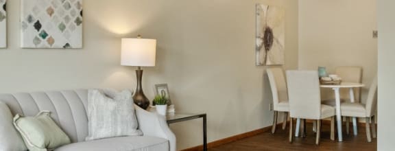 A living room with a white couch, a glass coffee table, and a painting on the wall at Point of America Apartments, Brooklyn Park, MN 55443