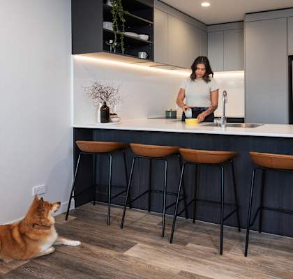 a woman preparing food in a kitchen with a cat laying on the floor