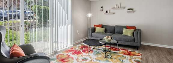 A living room with a grey couch, a black chair and a floral rug.