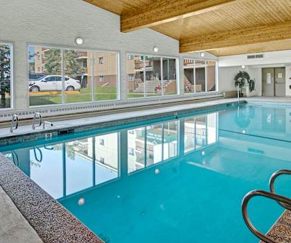 The indoor pool with a large window showing the parking lot and buildings of Wyndham Crossing Apartment Homes, and tables and chairs.