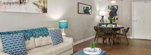 A living room with a white couch, a blue coffee table, and a painting on the wall.