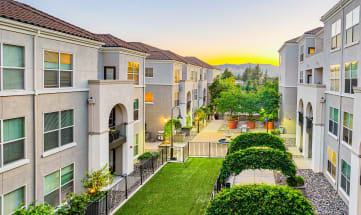 an aerial view of an apartment complex with a green courtyard and a sunset in the background