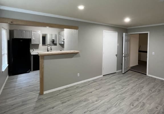 an empty living room with a kitchen in the background at The Lodge Apartments, Tulsa