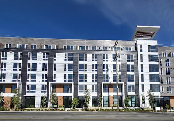 A large, modern multi-story building with a flat roof and a mix of grey and white exterior.