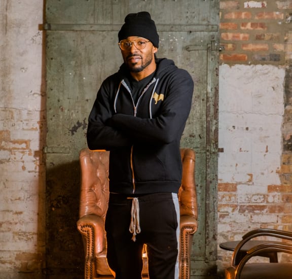 a man wearing a black hoodie and jeans standing in a brick room