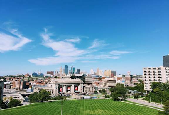 A cityscape with a large building in the center and a green field in the foreground.