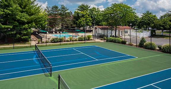 A tennis court with a net and trees in the background. at Quail Ridge, Plainsboro Township, NJ, 08536